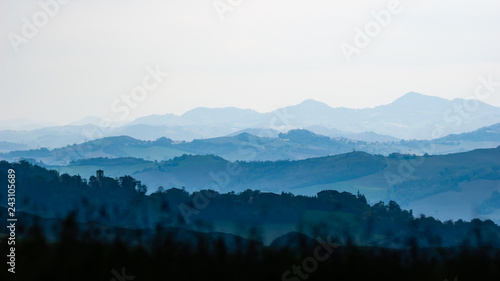 The meadows and the hills of the Montefeltro between Pesaro and Urbino, Italy, covered by trees in the shadow. The landscape disapears in the far distance haze