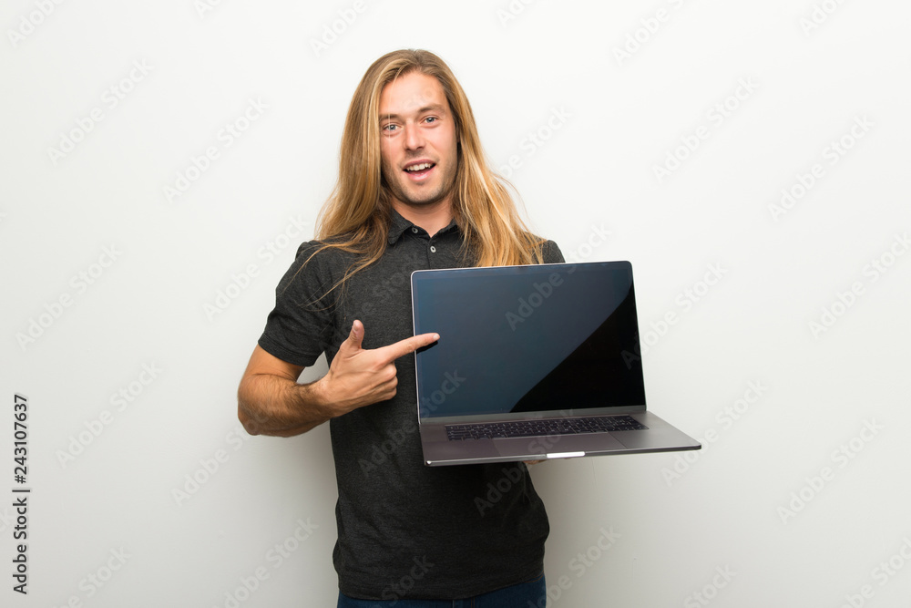 Blond man with long hair over white wall showing a laptop Blond man with long hair over white wall showing a laptop