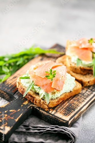Green cream cheese, salmon and arugula sandwich on a wooden board. Smorrebrod