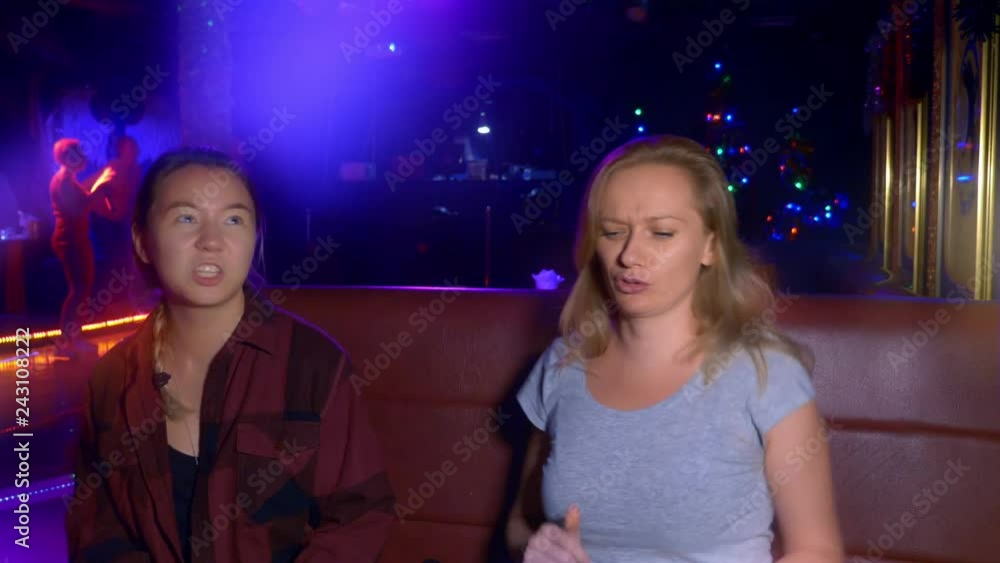 Two smiling young women Asian and Caucasian at a table in a nightclub Two smiling young women Asian and Caucasian at a table in a nightclub