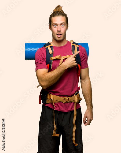 Hiker man with mountain backpacker surprised and pointing side on isolated background