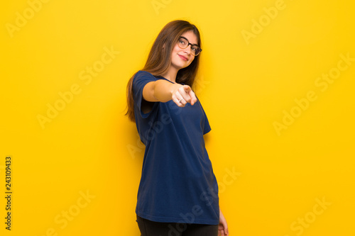Young woman with glasses over yellow wall points finger at you with a confident expression © luismolinero