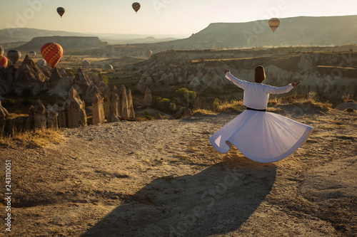 Dervish doing the retual in love valley of Cappadocia with balloons in background at sunrise.