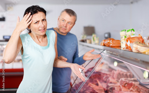 Sad couple customers choosing meat in shop