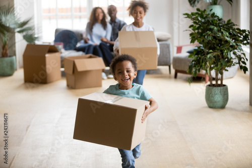 Cute happy mixed race children enjoying moving day running carrying holding boxes, excited african american kids laughing playing in new home having fun unpacking, black family relocation concept