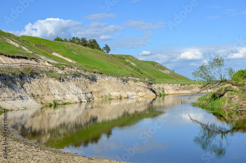 Spring countryside scenery with green hills and sky reflected in blue water surface.