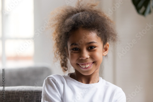 Cute funny little african american girl looking at camera, smiling mixed race child posing for portrait at home, preschool positive black kid with happy face headshot, orthodontic malocclusion photo