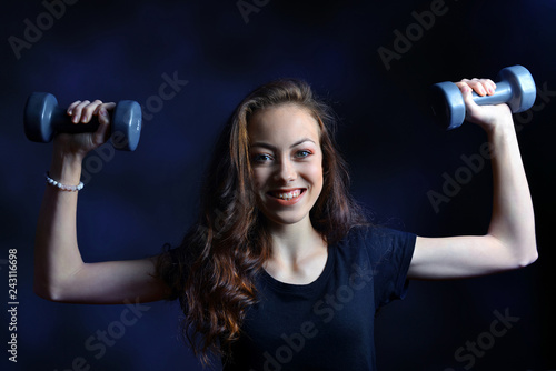 Beautiful caucasian girl holding in hands the dumbbells on dark background.