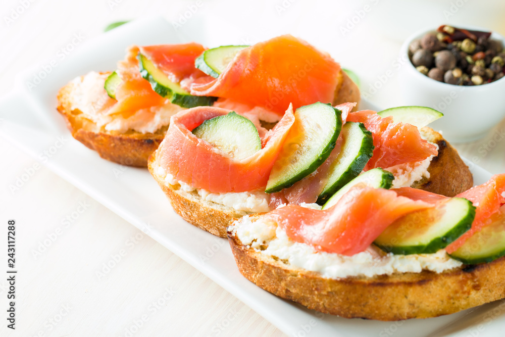 Salmon, cucumber and cream cheese bruschetta. Italian tapas, antipasti with vegetables, herbs and oil on grilled ciabatta and baguette bread. Sandwich.