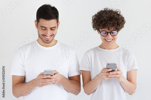 Young couple holding mobile phones and standing together isolated on gray background