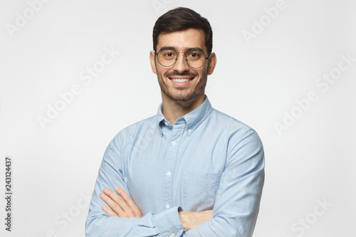 Modern businessman in blue shirt standing with crossed arms, isolated on gray background