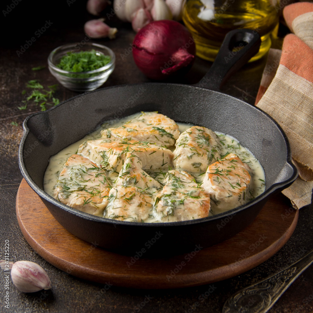 Chicken fillet or Turkey breast in creamy sauce with dill and garlic, in cast iron black pan on dark background. Delicious homemade food Chicken fillet or Turkey breast in creamy sauce with dill and garlic, in cast iron black pan on dark background. Delicious homemade food