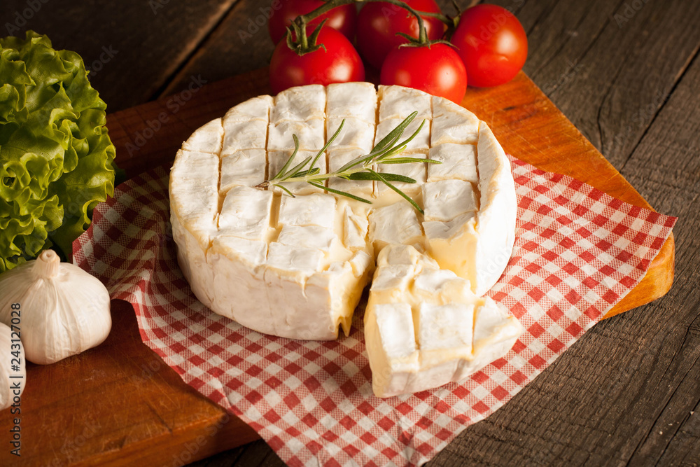 Camembert and brie cheese on wooden background with tomatoes, letuce and garlic. Italian food. Dairy products. Camembert and brie cheese on wooden background with tomatoes, letuce and garlic. Italian food. Dairy products.