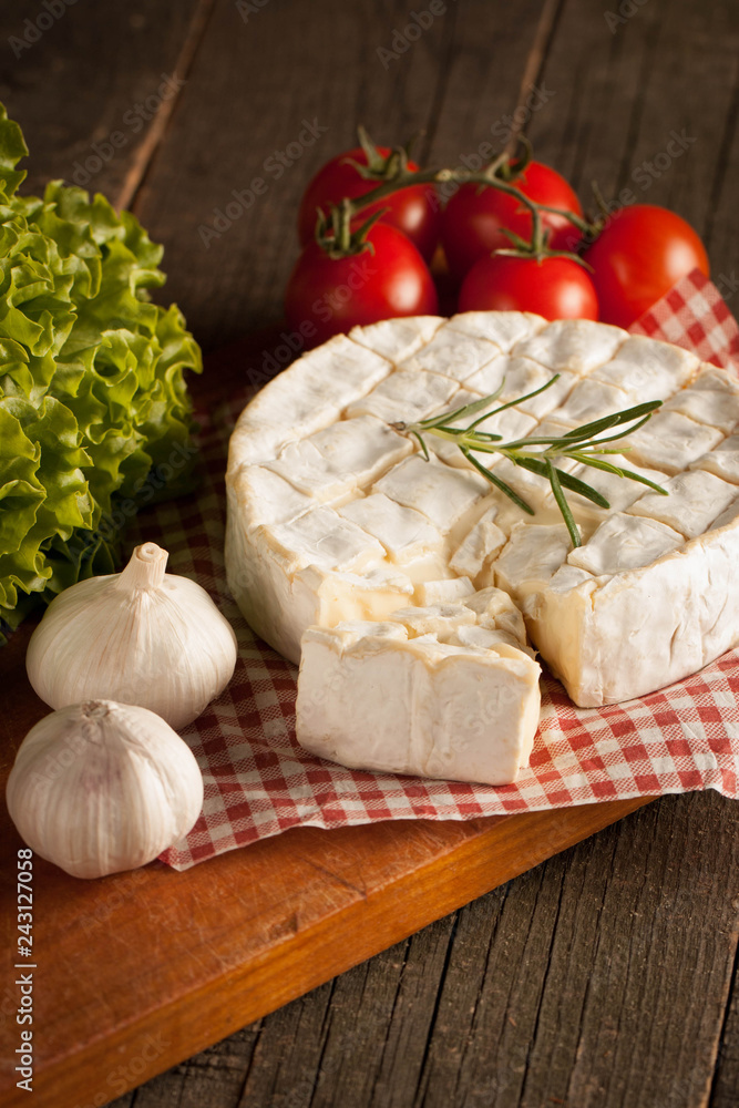 Camembert and brie cheese on wooden background with tomatoes, letuce and garlic. Italian food. Dairy products. Camembert and brie cheese on wooden background with tomatoes, letuce and garlic. Italian food. Dairy products.