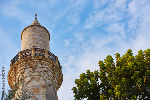 Top of the minaret of the mosque against the blue sky with a green tree