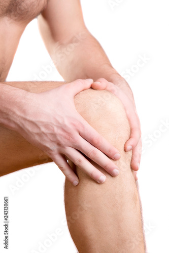 A man touches a sore knee on a white background.