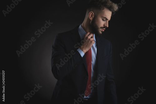 portrait of businessman looking down to side and fixing tie