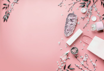 Cosmetic concept. Facial skin care products and paper shopping bag on pastel pink background with cherry blossom and leaves, top view, frame. Copy space for your design. Beauty blog layout. Flat lay