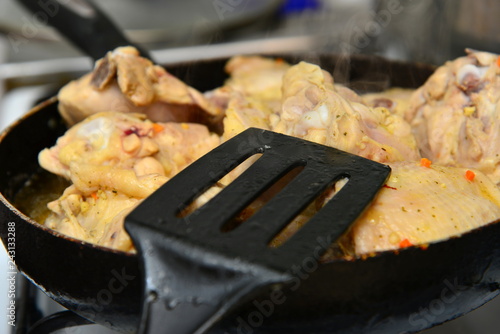 The cook mixes fried chicken in a pan with butter and spices.