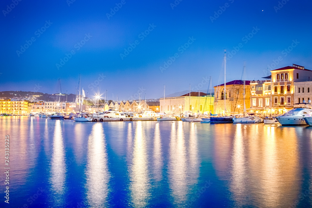Beautiful Night Panorama of Old Venetian City of Chania Taken at Blue Hour from Pier with Yachts and Boats in Foreground.