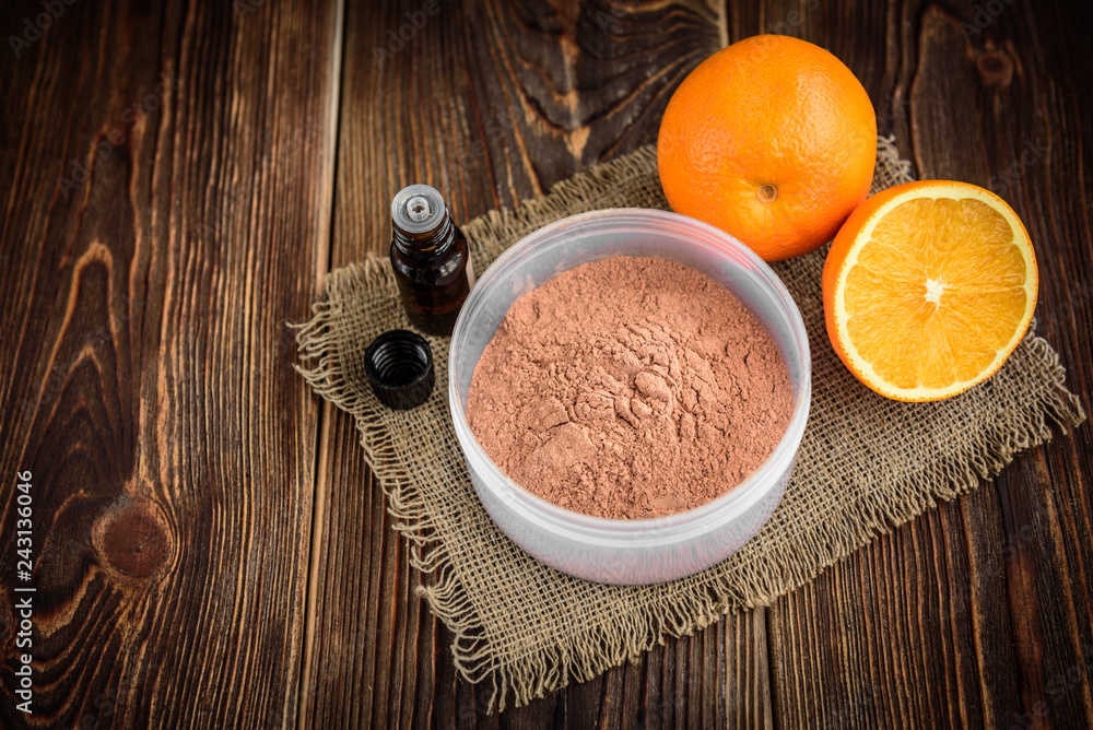Pink cosmetic clay, essential oil and oranges on dark wooden background. Ingredients for mask- cosmetic clay, aroma oil, orange. Homemade skincare. 