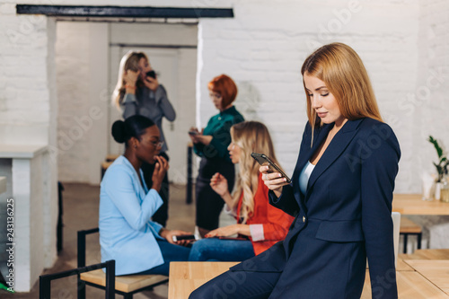 Confident caucasian woman speaking on smartphone and looking at camera, trying to solve client problem while group of people sitting on background