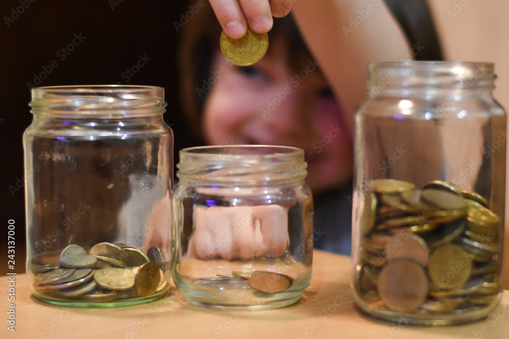 Boy putting coins in a glass jar. Concept of saving. Child save money for Christmas presents Boy putting coins in a glass jar. Concept of saving. Child save money for Christmas presents