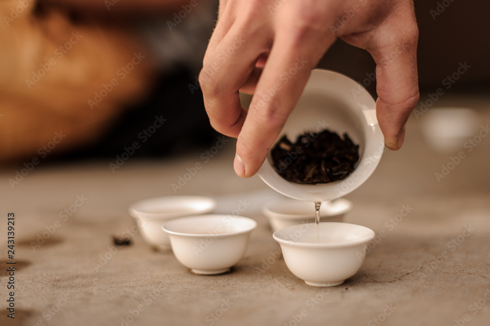 Male hand pouring fresh tea from porcelain cup into small pots Male hand pouring fresh tea from porcelain cup into small pots