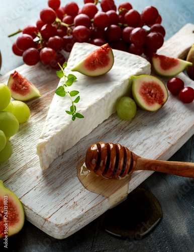 Cheese brie with figs, green and red grape and honey on white wooden board