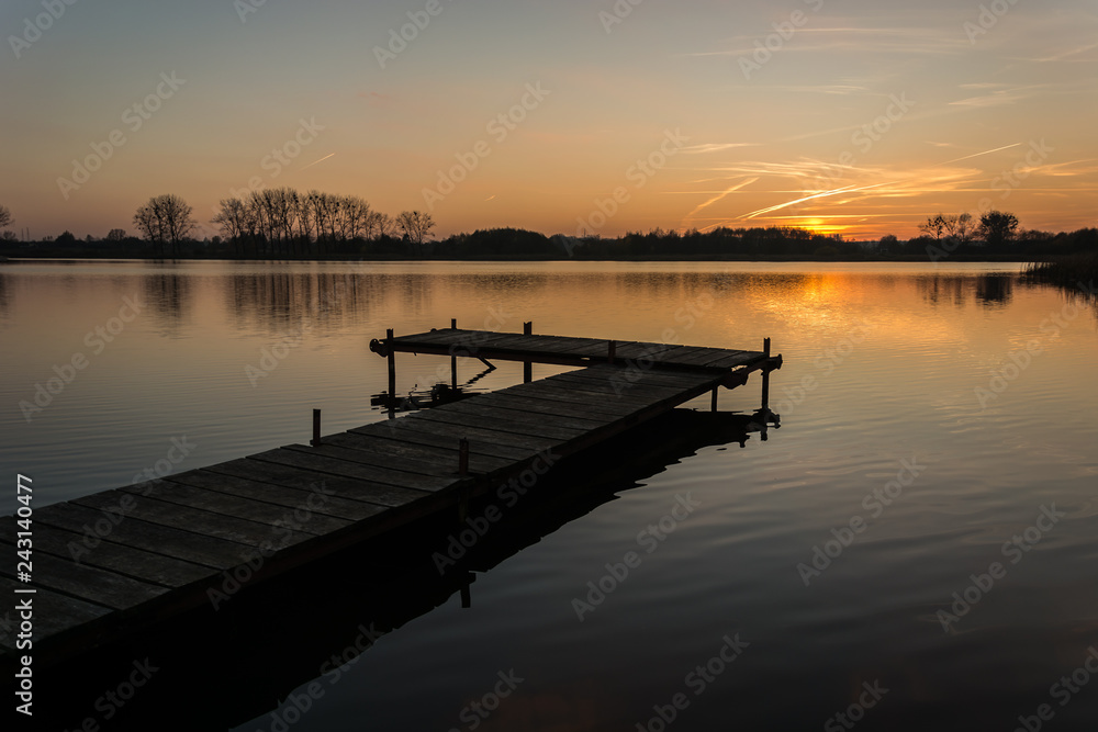 Fototapeta premium Long jetty on a calm lake and the sky during sunset.