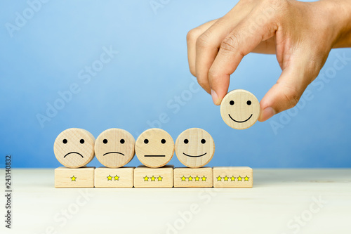 Customer service evaluation and satisfaction survey concepts. The client's hand picked the happy face smile face icon and five star symbol on wooden cube on table photo