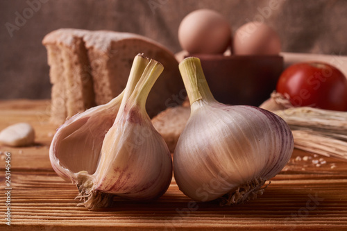 garlic on a wooden table with eggs in clay bowl, tomato, battledore and wheat sprouts