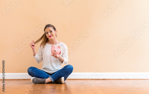 Young woman with a piggy bank against a big interior wall