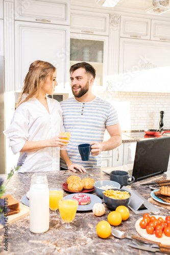 Waist up portrait of loving young couple enjoying morning at home while looking tenderly at each other standing at kitchen counter