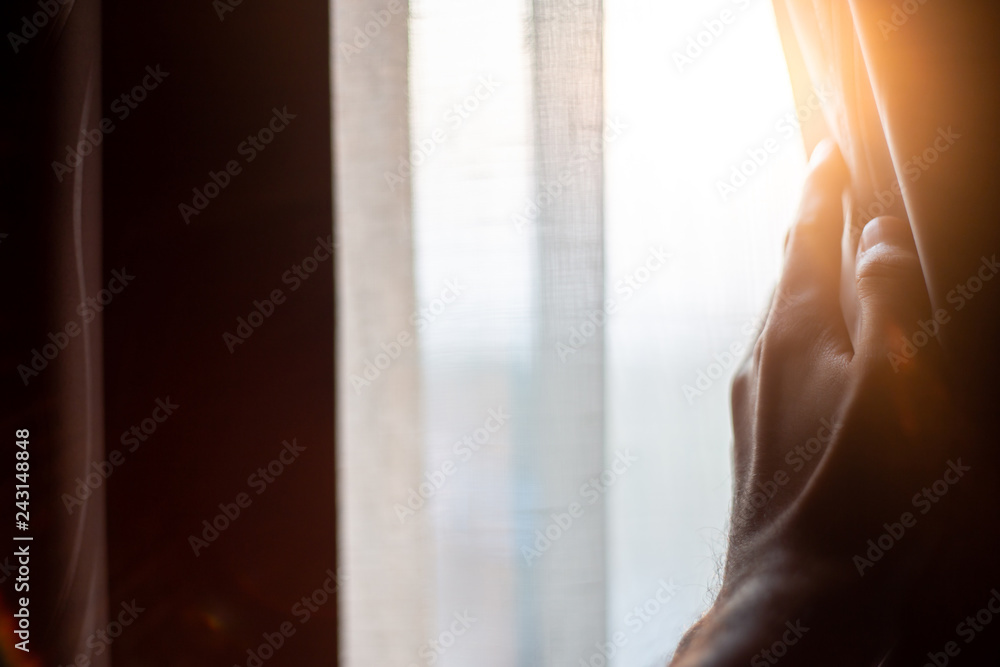Hand opening curtains in the bedroom with sun light background