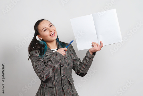 portrait of a woman in a jacket on a light background. holding a notebook with a copy space and shows pen.