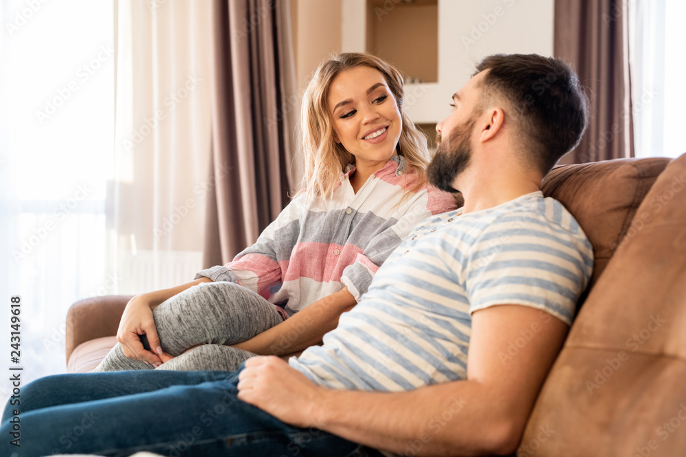Portrait of happy couple talking to each other while relaxing sitting on sofa at home, focus on smiling beautiful woman looking at husband with love Portrait of happy couple talking to each other while relaxing sitting on sofa at home, focus on smiling beautiful woman looking at husband with love