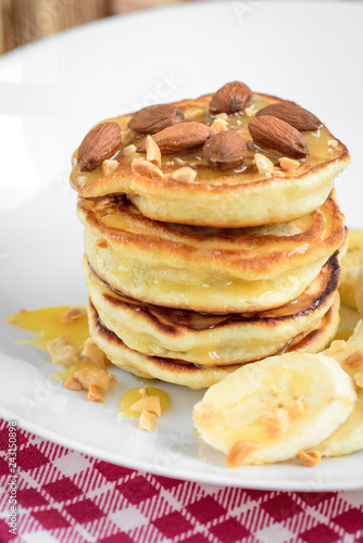 Pancakes with banana,nuts and honey on white plate for breakfast on wooden background with copy space.