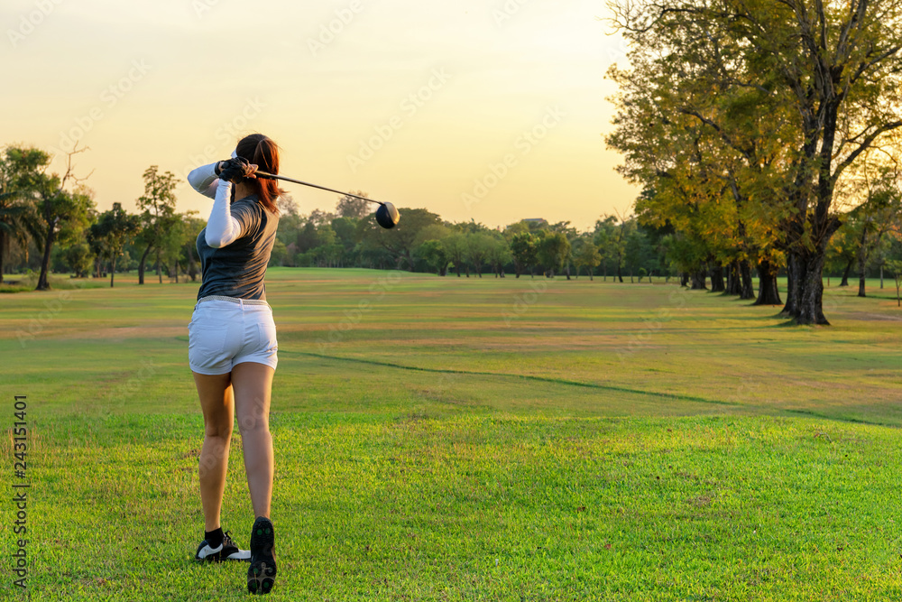 Healthy Sport. Asian Sporty woman golfer player doing golf swing tee off on the green evening time, she presumably does exercise.  Healthy Lifestyle Concept.