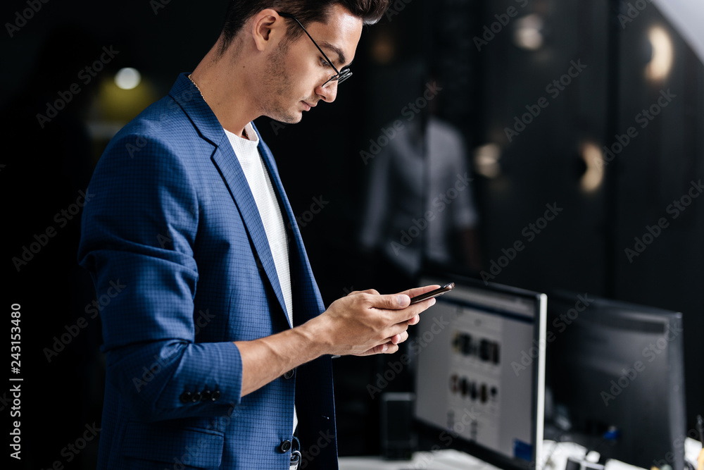 Professional young architect in glasses dressed in blue checkered jacket uses the phone in the office Professional young architect in glasses dressed in blue checkered jacket uses the phone in the office