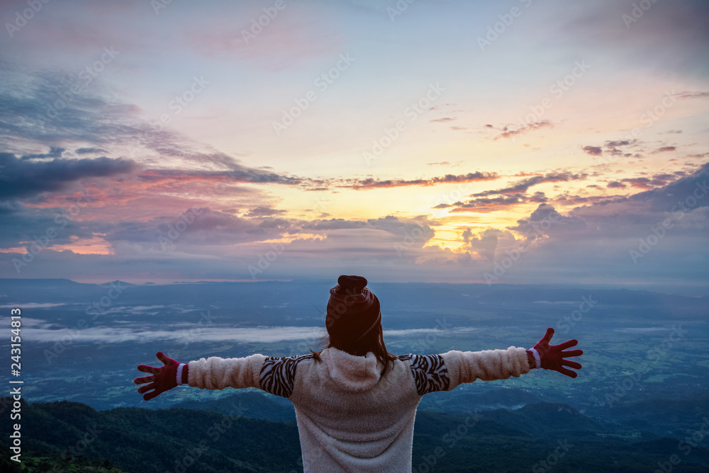Fototapeta premium Woman tourist in a sweater dress outstretched arms, happy while watching the beautiful nature landscape of the forest and mountain during the sunrise at Phu Thap Boek Viewpoint Phetchabun, Thailand