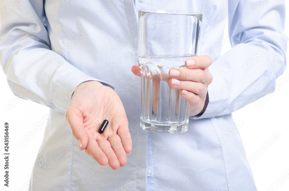 Black capsule pill and glass of water medicine in woman hand on white background, pharmacy concept Black capsule pill and glass of water medicine in woman hand on white background, pharmacy concept