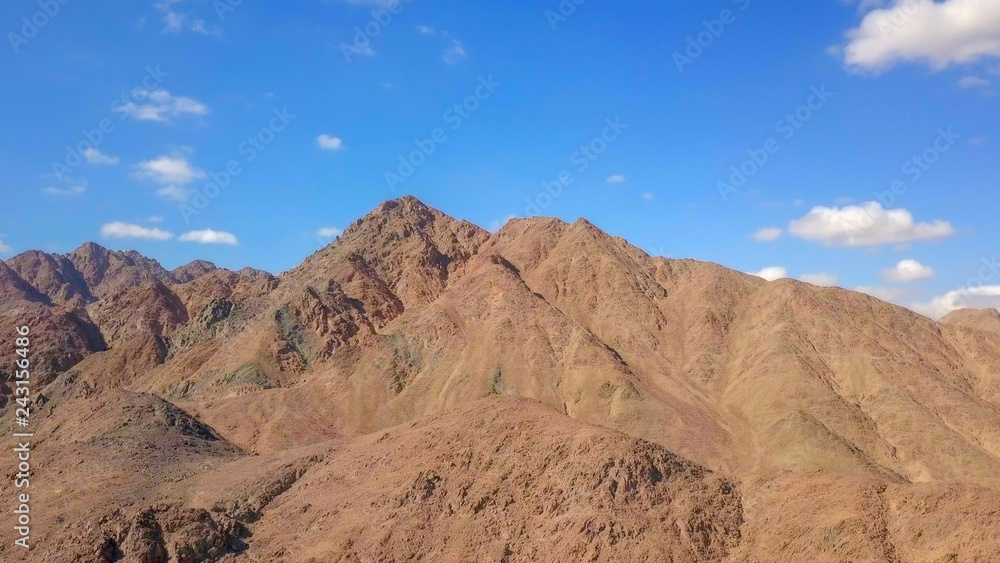 Desert landscape - Aerial image of mountains and dry land with blue cloudy sky in the background.