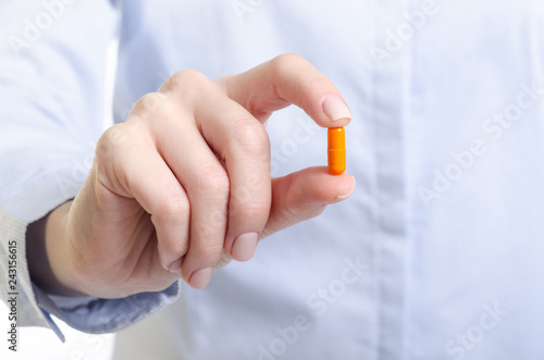 Orange capsule pill medicine in woman hand on blur background, pharmacy concept