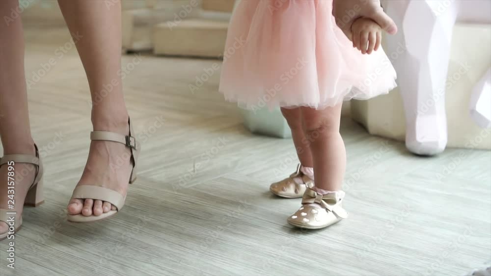 Feet of toddler baby taking first steps with mother help at special event like wedding or birthday party Feet of toddler baby taking first steps with mother help at special event like wedding or birthday party