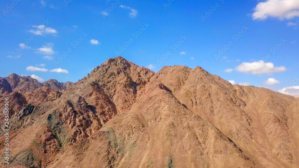 Desert landscape - Aerial image of mountains and dry land with blue cloudy sky in the background.