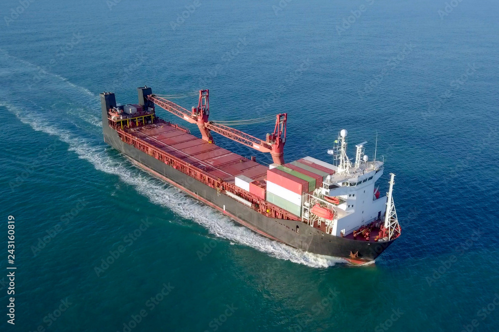 Large Cargo and RoRo (Roll On-Off) ship at sea, loaded with a small amount of shipping containers and two large cranes - Aerial image following the ship.