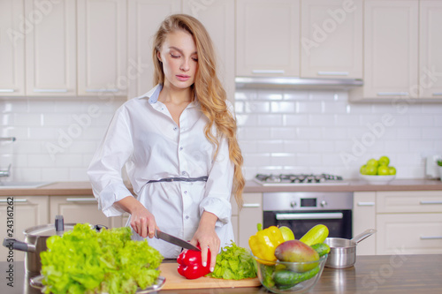 Beautiful girl in a white shirt prepares vegetables in the kitchen
