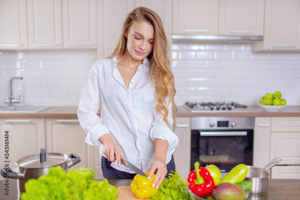 Beautiful girl in a white shirt prepares vegetables in the kitchen Beautiful girl in a white shirt prepares vegetables in the kitchen