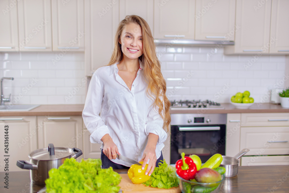 Beautiful girl in a white shirt prepares vegetables in the kitchen Beautiful girl in a white shirt prepares vegetables in the kitchen